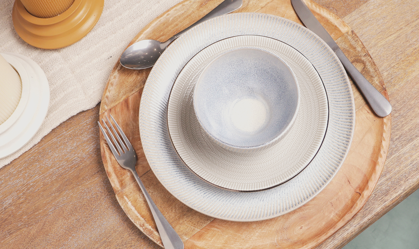 Minimal ceramic plates styled on a wooden dining table with cutlery.